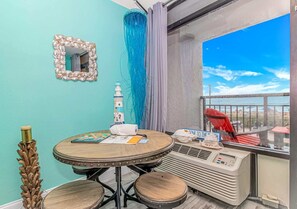 A room with a round table, a small white object resembling a lighthouse, a decorative mirror, and a view of the sea through a window.