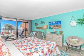 A bedroom with a bed, a dresser, a chair, and a balcony with a view.