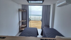 A hotel room with two beds, a desk, a wardrobe, and a view of the beach. - Hibisco Guest House (Florianopolis)