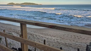 A beach with a wooden railing, sandy shore, and waves. - Hibisco Guest House (Florianopolis)