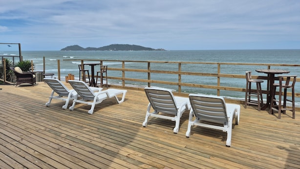 A wooden deck with white lounge chairs and tables overlooking the ocean. - Hibisco Guest House (Florianopolis)