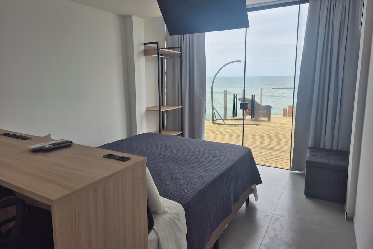 A hotel room with a bed, a desk, and a view of the beach.