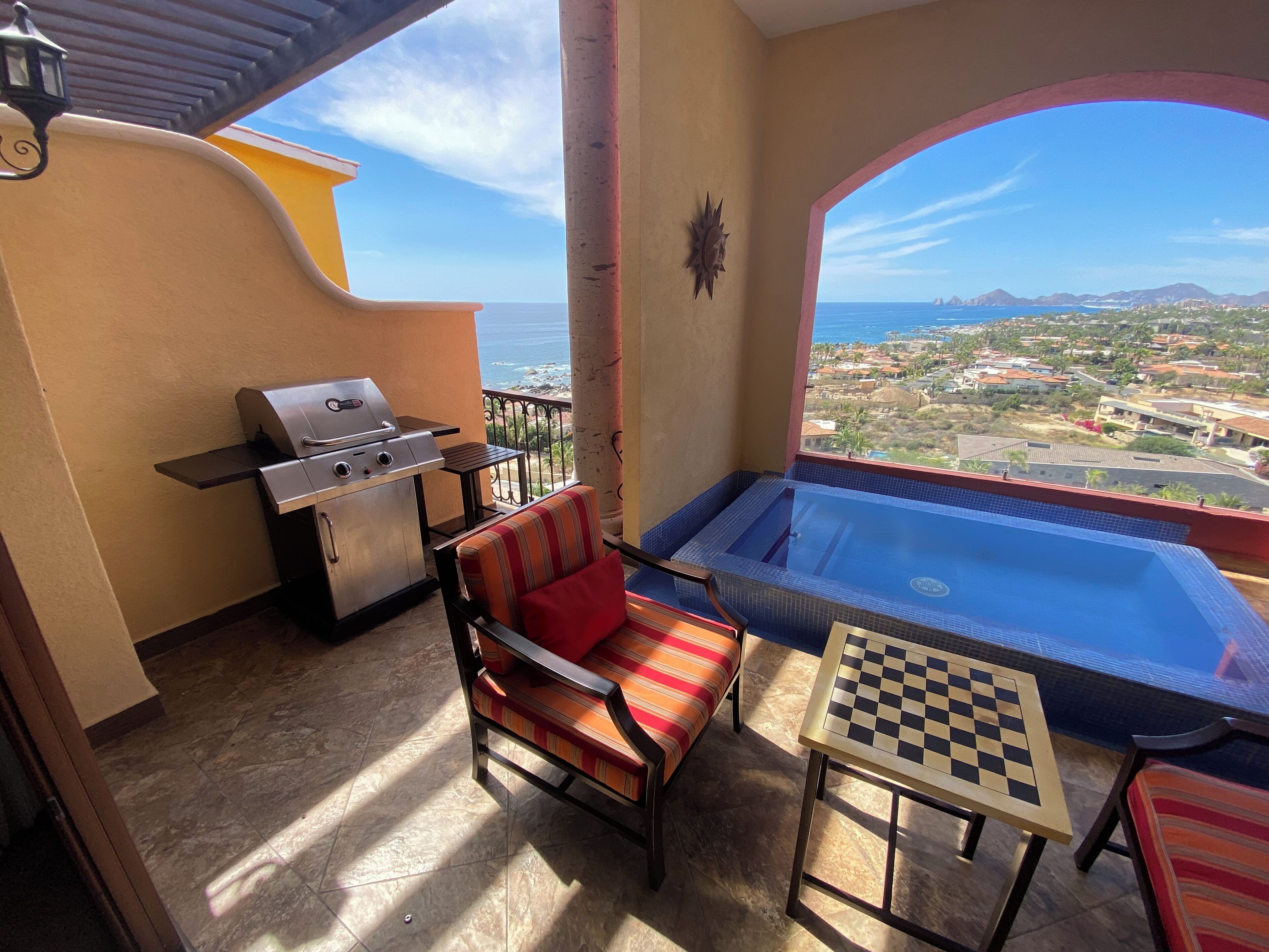 A balcony with a grill, a cushioned chair, a small table, and a hot tub.