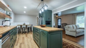A modern kitchen with wooden cabinets, a central island, and a dining area with a table and chairs. - Comfort & Space in Prime Cartersville Spot (Cartersville)