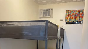A bunk bed with a mesh top and a single mattress, a small window with colorful curtains, and a wooden floor.