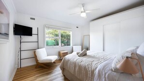 Un dormitorio con una cama, una silla, un televisor y una ventana.