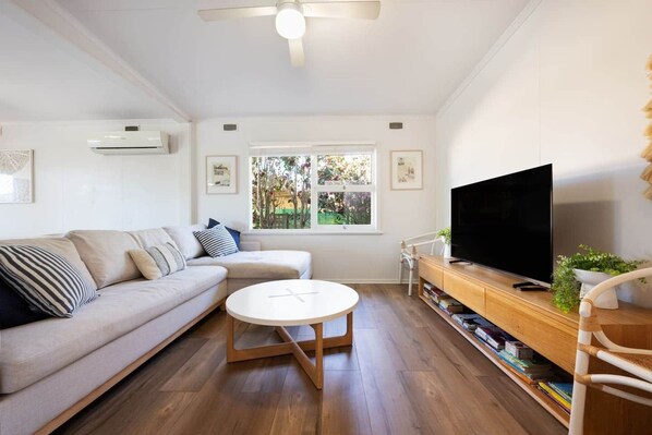 A living room with a sofa, a round coffee table, a TV on a wooden stand, and a bookshelf.