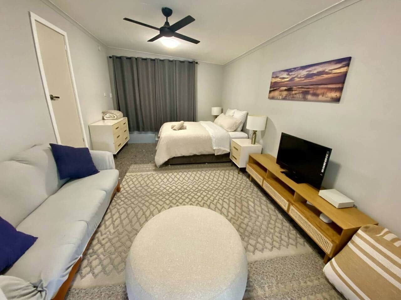 Una habitación de hotel con cama, sofá, televisor, una mesita y ventilador de techo.