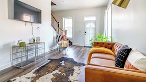 A modern living room with a flat-screen TV, a wicker chair, a leather sofa, and a cowhide rug. - Jungle House Downtown Columbus – Modern Boutique Suites (Columbus)
