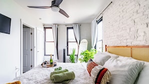 A bedroom with a bed, a ceiling fan, a window, and a plant. - Jungle House Downtown Columbus – Modern Boutique Suites (Columbus)