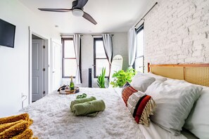 Un dormitorio con cama, ventilador de techo, ventana y una planta.