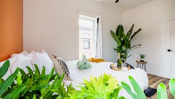 Een slaapkamer met een bed, een plafondventilator, een raam en verschillende planten.