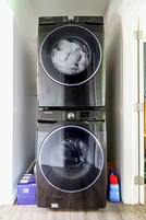 Two stacked Samsung washing machines in a room with a wooden floor and a white door.