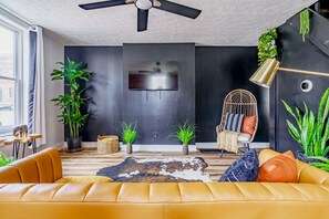 A modern living room with a sofa, a television, and various plants. - Jungle House Downtown Columbus – Modern Boutique Suites (Columbus)