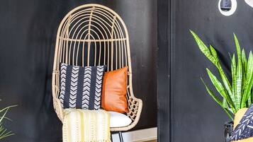 Un intérieur moderne avec un mur noir, un fauteuil en osier agrémenté de coussins à motifs, un canapé jaune et des plantes vertes.