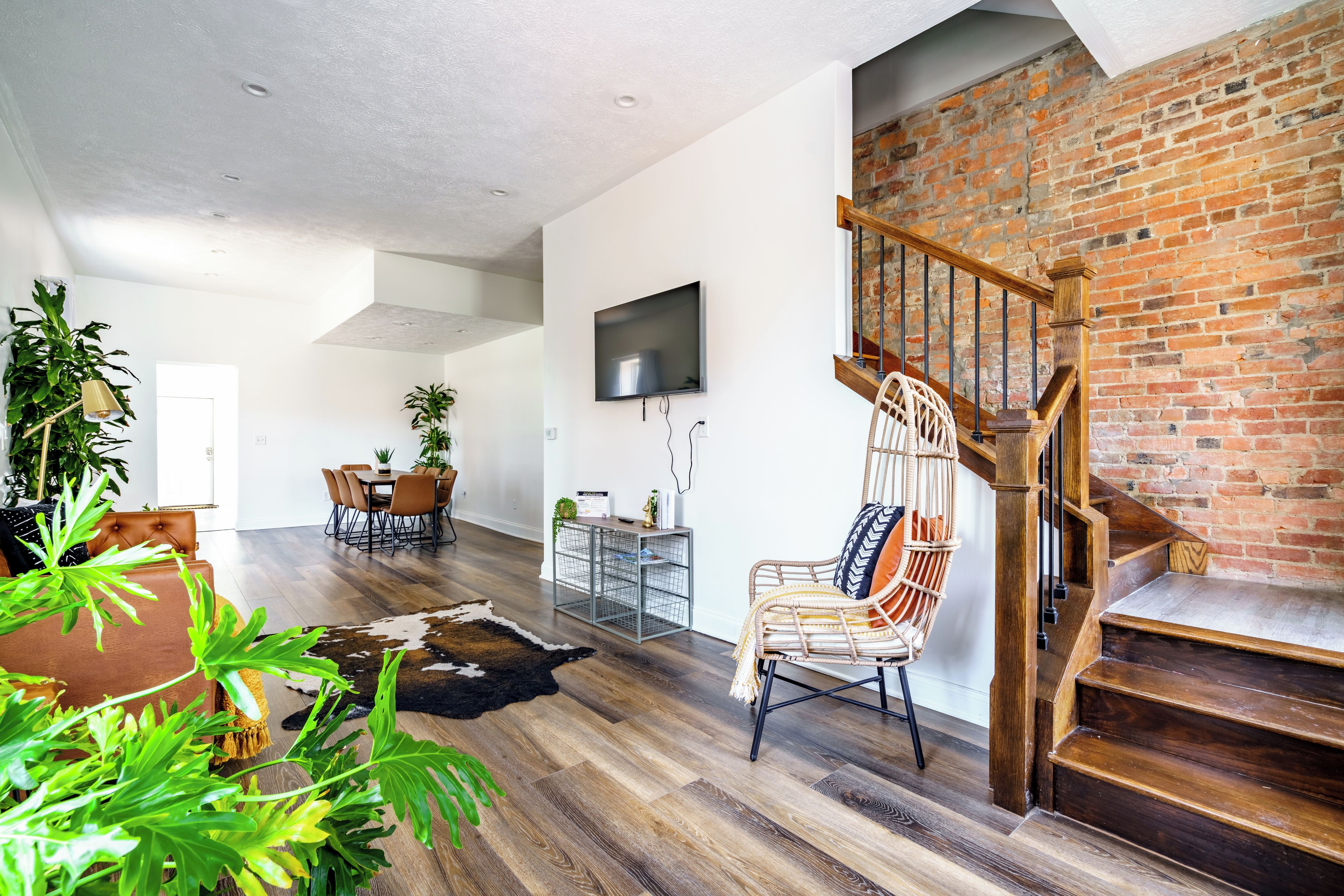 A spacious living area with a wooden staircase, a dining table with chairs, and a TV mounted on the wall.
