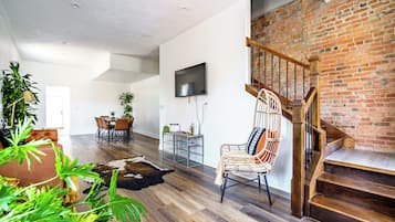 A spacious living area with a wooden staircase, a dining table with chairs, and a TV mounted on the wall.