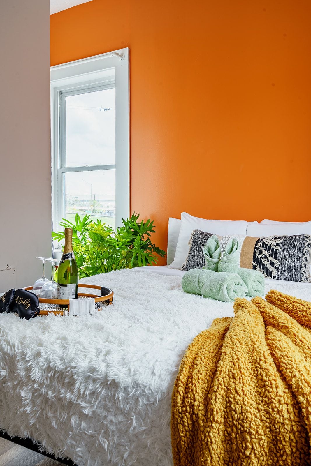 Une chambre avec un lit blanc moelleux, des murs orange, une fenêtre et une plante.