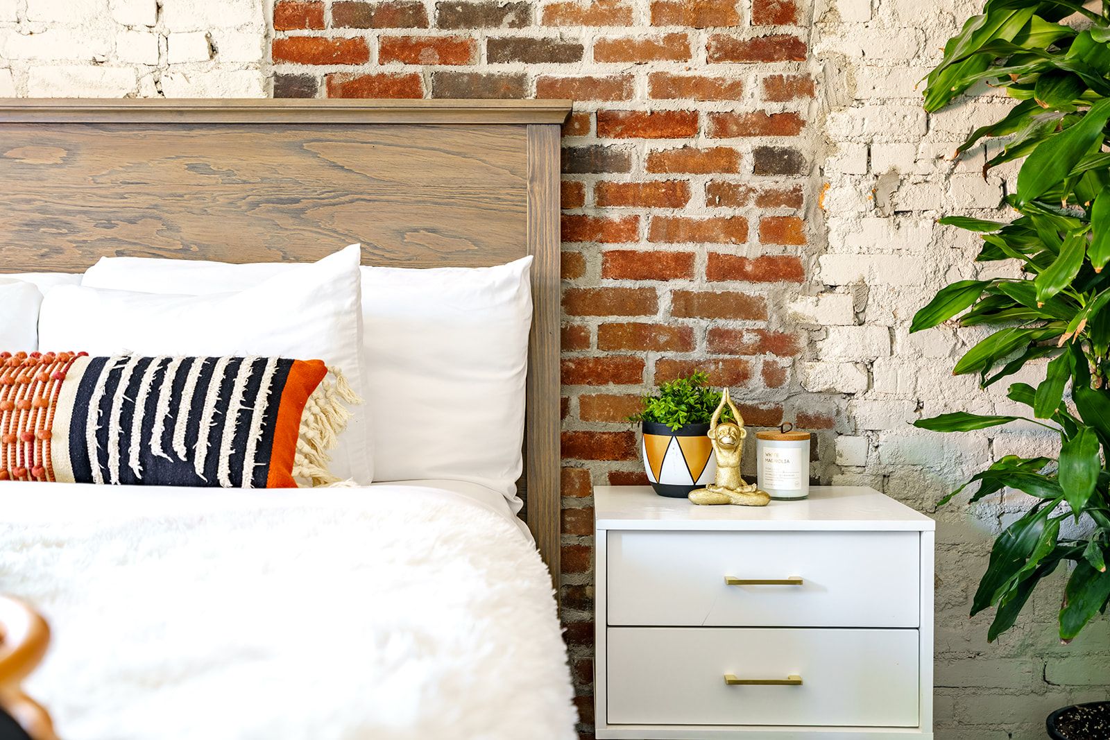 A bed with white bedding, a striped pillow, and a nightstand with a plant and a small statue.