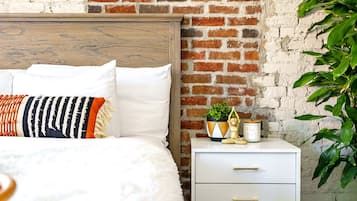 A bed with white bedding, a striped pillow, and a nightstand with a plant and a small statue.