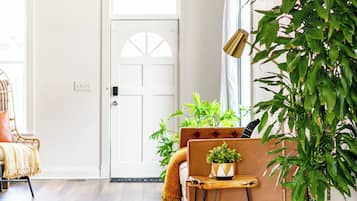 A room with a wooden floor, a sofa, a small table with a plant, and a potted plant by the window.