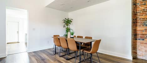 A dining area with a wooden table and chairs, a potted plant, and a brick wall.