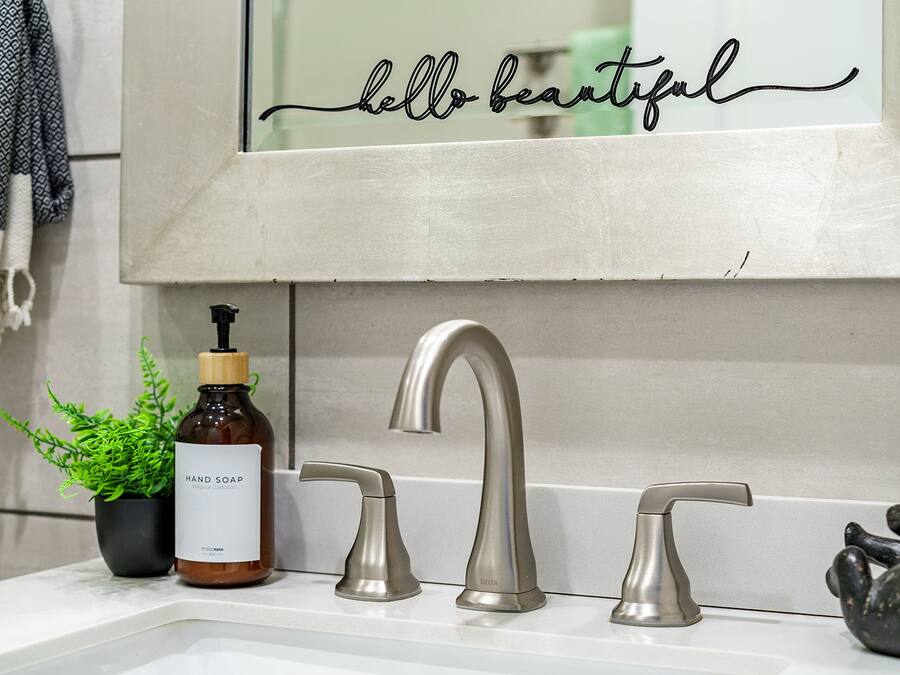Een badkamer met een wastafel, een handzeepfles, een potplant en een decoratieve wand met de tekst 'hello beautiful'.