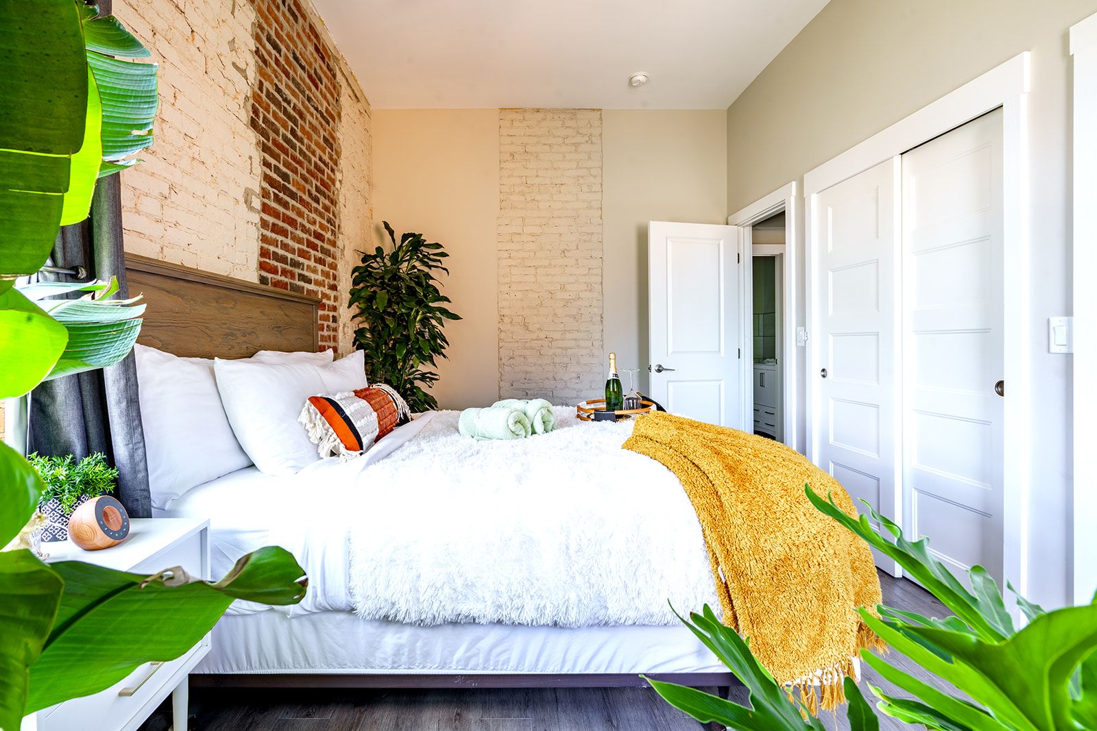 Une chambre à coucher avec un lit, une plante, une porte et un mur en briques.