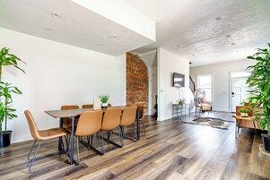 A modern dining area with a brick wall, a wooden dining table, and leather chairs.