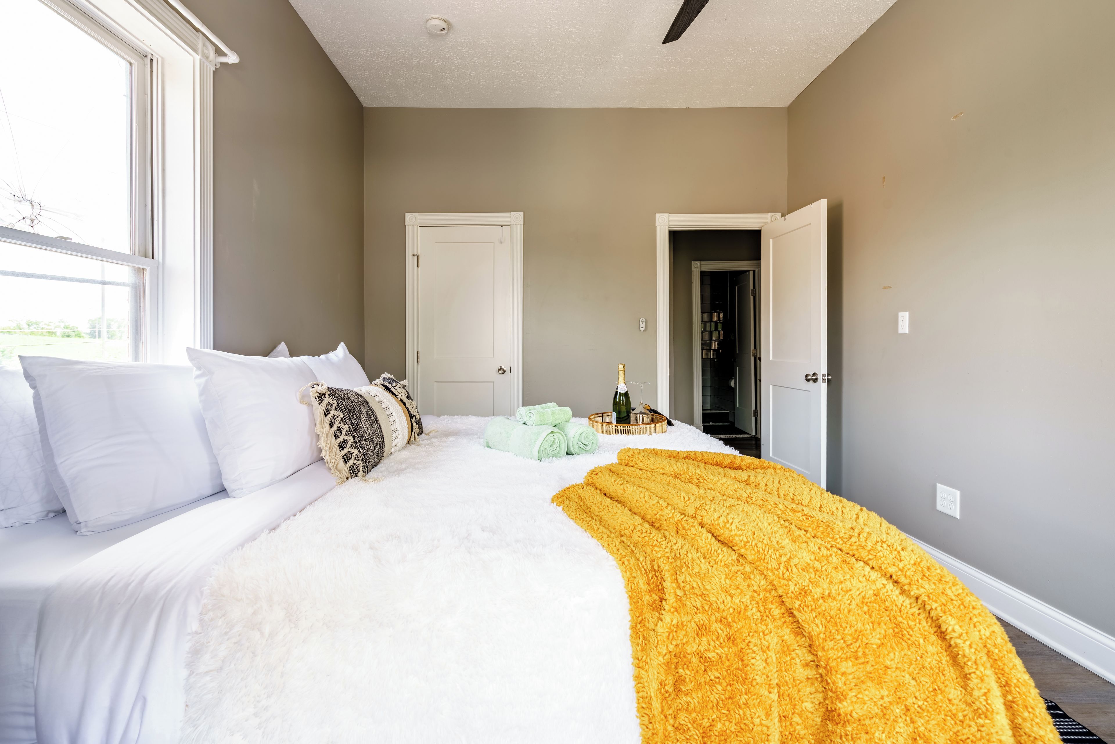 A bedroom with a large bed, a white door, and a view of a hallway.