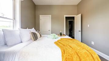 A bedroom with a large bed, a white door, and a view of a hallway.