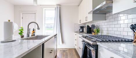 A modern kitchen with white cabinetry, a stainless steel range hood, and a black countertop.