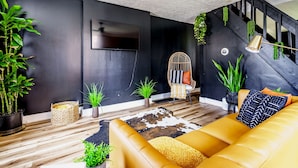 A modern living room with a sofa, a chair, a TV, and plants. - Jungle House Downtown Columbus – Modern Boutique Suites (Columbus)