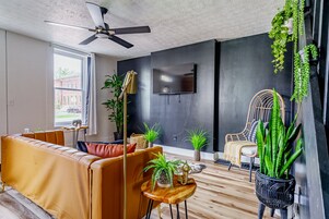 Una sala de estar moderna con un sofá, un ventilador de techo, un televisor y diversas plantas.