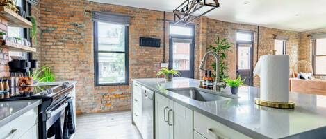 Una cocina moderna con pared de ladrillo, electrodomésticos de acero inoxidable y una isla grande con lavamanos.