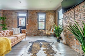A cozy living room with a brick wall, a leather sofa, a coffee table, and a large plant. - Jungle House Downtown Columbus – Modern Boutique Suites (Columbus)