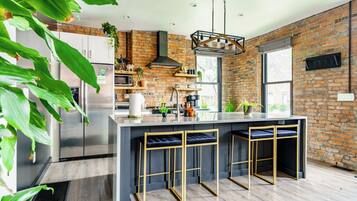 A modern kitchen with a central island, bar stools, a brick wall, and a large window.
