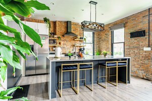 A modern kitchen with a central island, bar stools, a brick wall, and a large window.