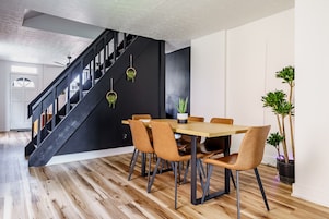Un comedor con mesa de madera y sillas de cuero, una escalera negra y plantas en macetas.