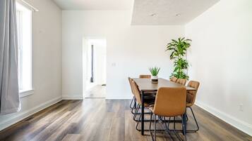 A modern dining room with a wooden table and chairs, a potted plant, and a view of a hallway.