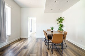 A modern dining room with a wooden table and chairs, a potted plant, and a view of a hallway. - Jungle House Downtown Columbus – Modern Boutique Suites (Columbus)