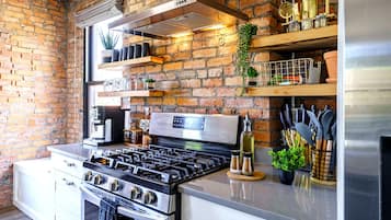 A kitchen with a brick wall, stainless steel appliances, and shelves with various items.