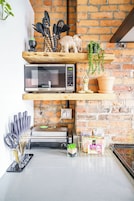 A kitchen with a brick wall, a microwave, a toaster, and various kitchen utensils on shelves.
