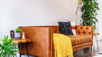 A brown leather sofa with a yellow throw blanket, a small side table with a plant, and a tall floor lamp.