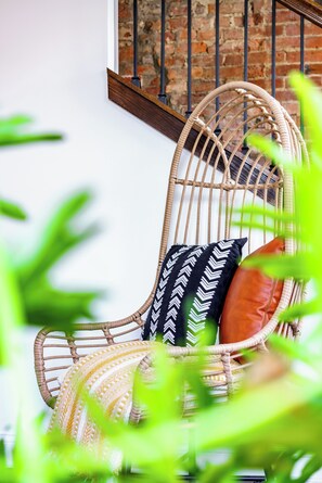 A wicker chair with patterned cushions against a brick wall, with a staircase in the background. - Jungle House Downtown Columbus – Modern Boutique Suites (Columbus)