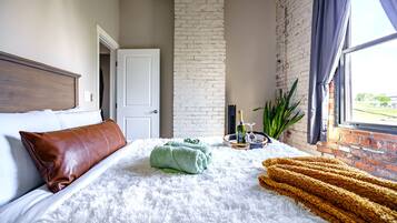 A hotel room with a bed, a brick wall, a window, and a door.