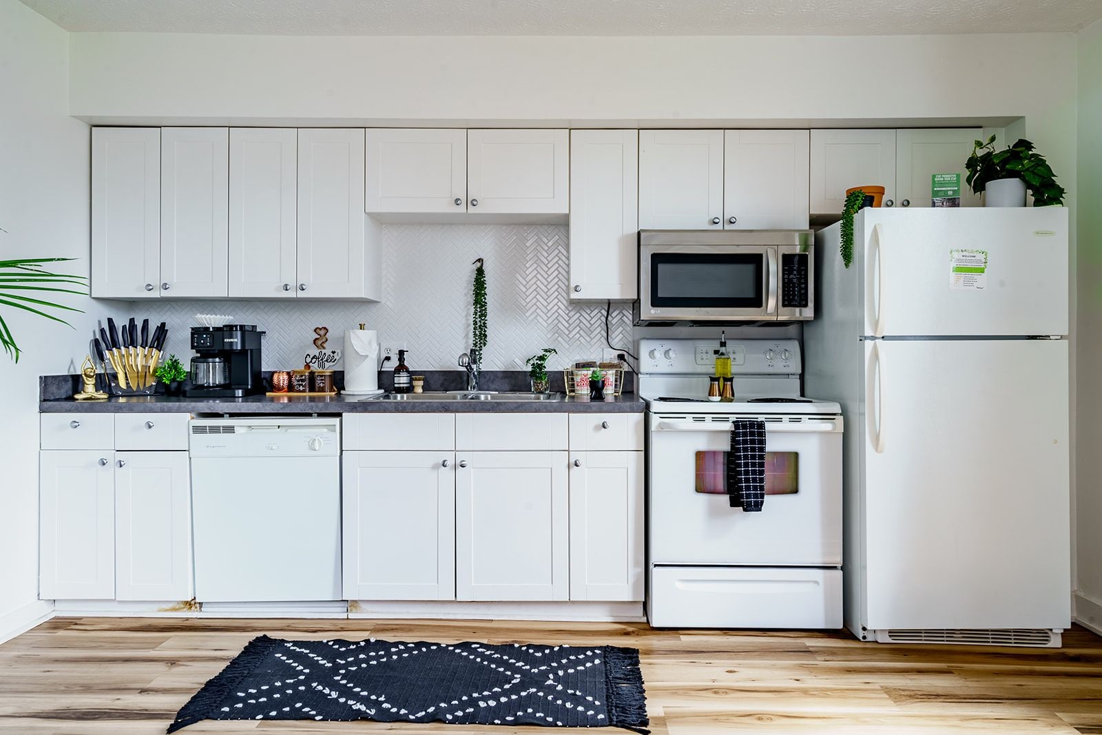 A kitchen with white cabinets, a microwave, a stove, a refrigerator, and a black rug.