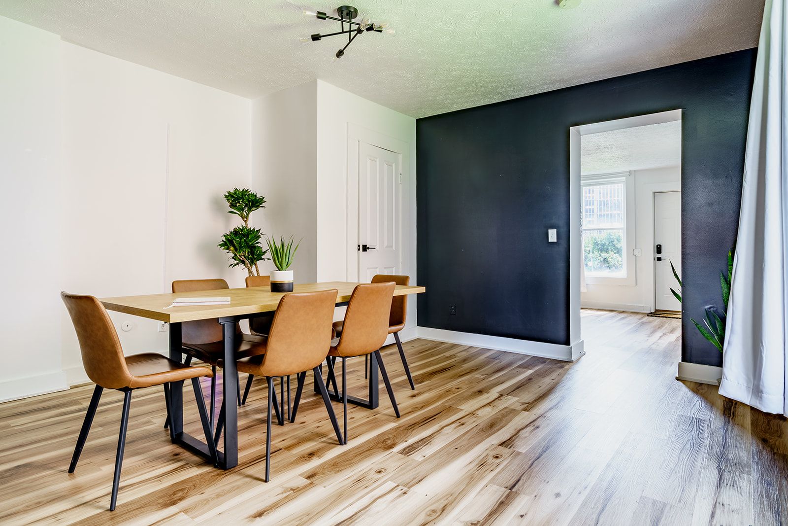 A dining area with a wooden table and chairs, a ceiling light fixture, and a dark wall.