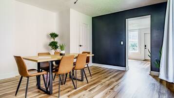 A dining area with a wooden table and chairs, a ceiling light fixture, and a dark wall.