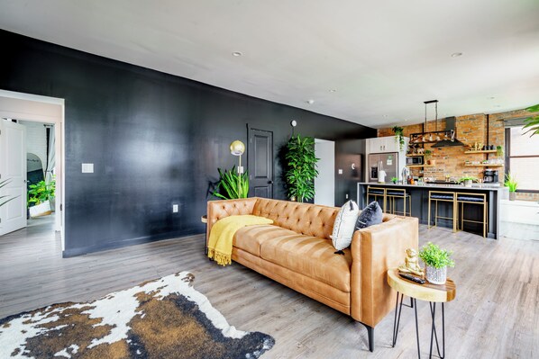 A modern living room with a leather sofa, a cowhide rug, and a small round table with a plant and a remote control. - Jungle House Downtown Columbus – Modern Boutique Suites (Columbus)
